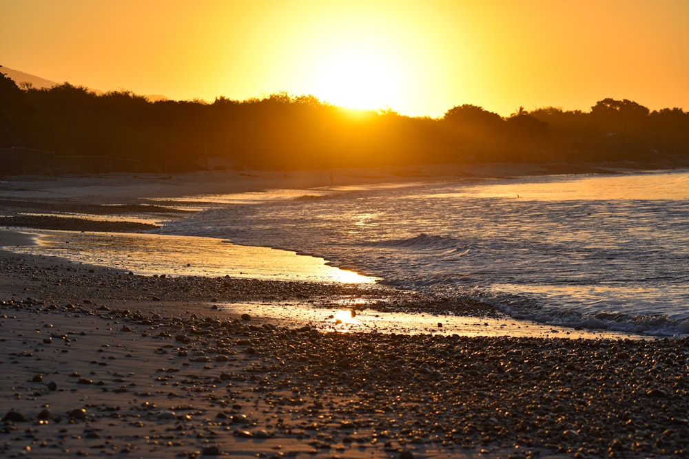 the sun is setting over the water at the beach