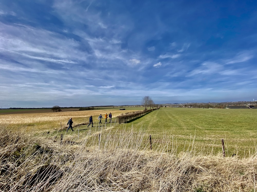 a group of people walking across a grass covered field