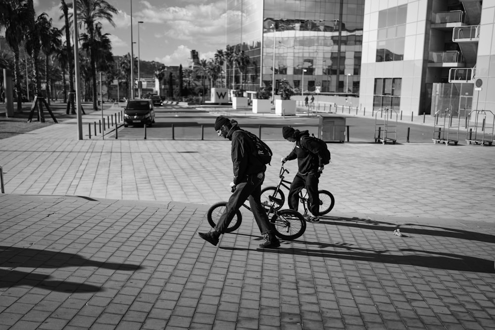 a couple of men riding bikes down a sidewalk