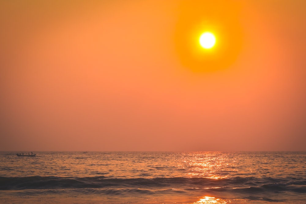 the sun is setting over the ocean with a boat in the distance