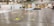 A large convention center hall arranged for an event setup with scattered boxes, crates, and equipment. There are partitions covered with white drapes, directional signs hanging from the ceiling, and yellow taped lines on the floor. A person is walking through the hall, and equipment is positioned sporadically.