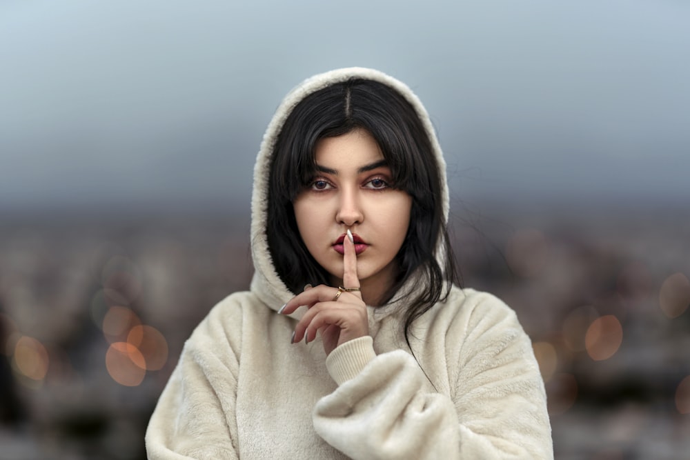 a woman in a hooded jacket is holding her finger to her lips