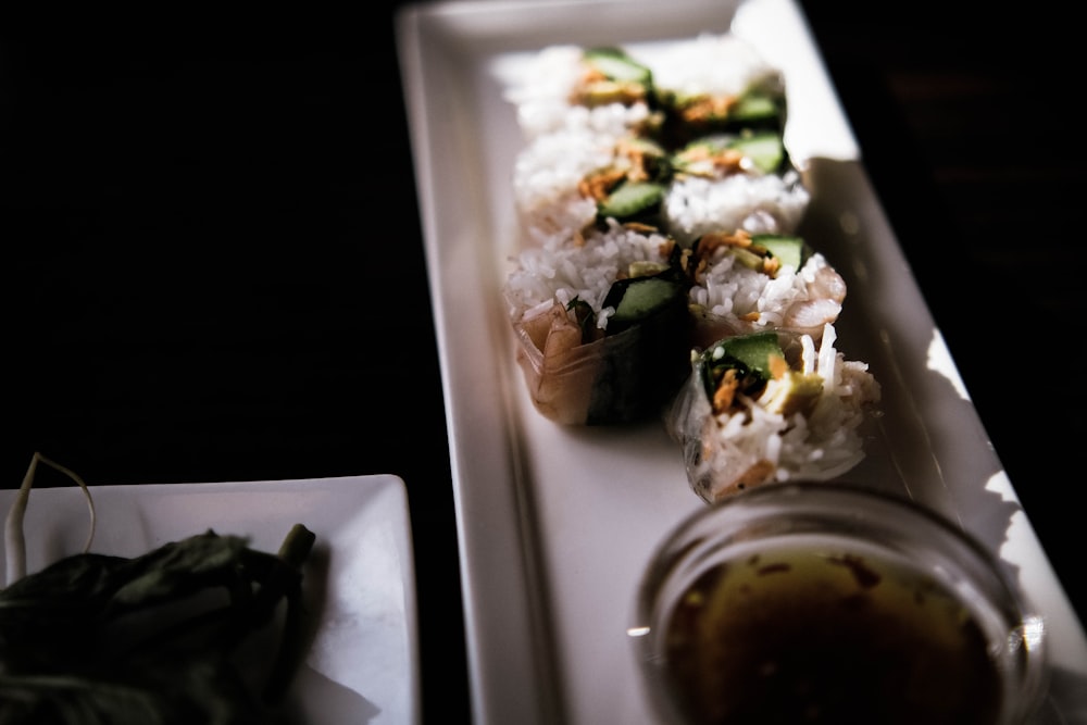 a white plate topped with sushi next to a bowl of sauce