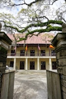 A historical museum building nestled among oak trees with informative plaques visible on the pathway.