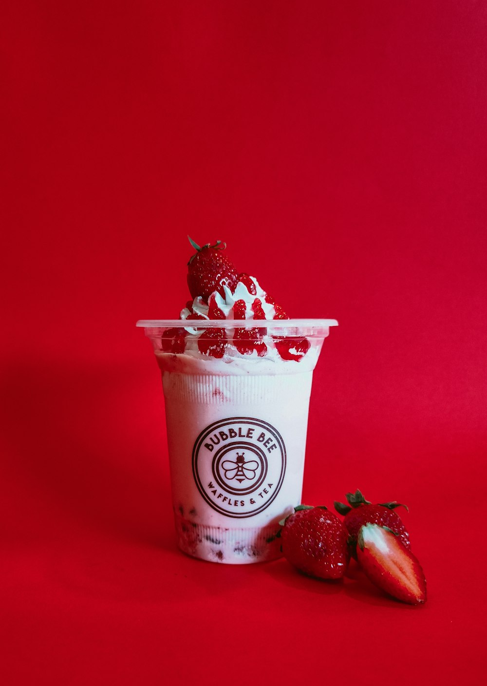 a cup of ice cream with strawberries on a red background
