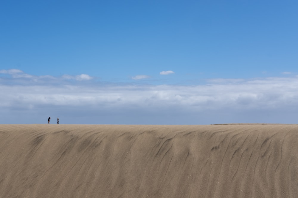 a couple of people standing on top of a sandy hill