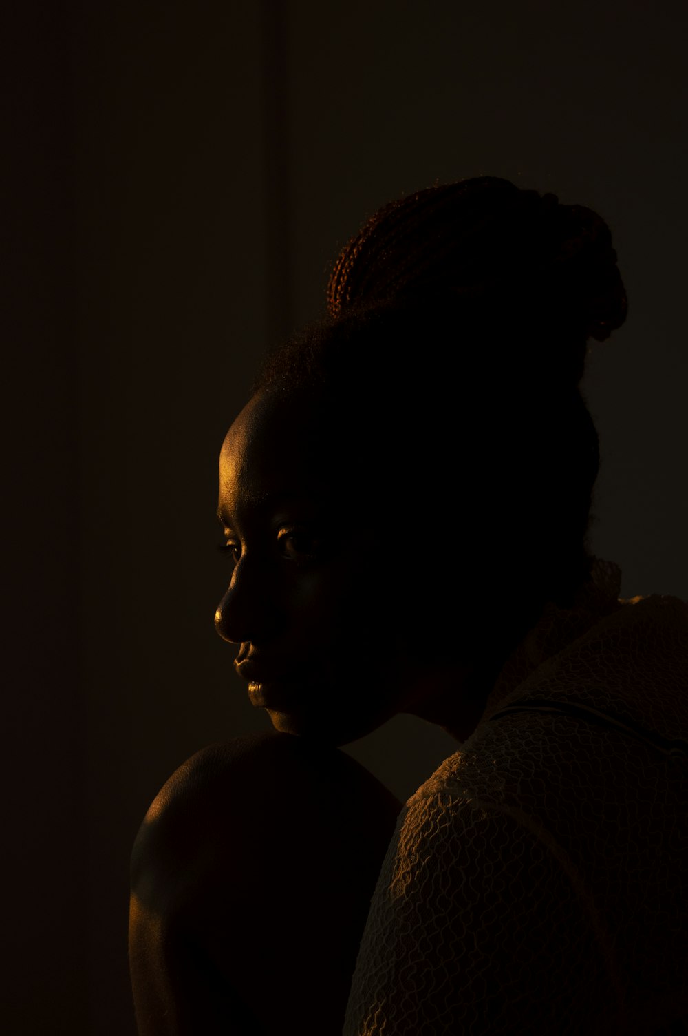 a woman sitting in a dark room with her head turned to the side