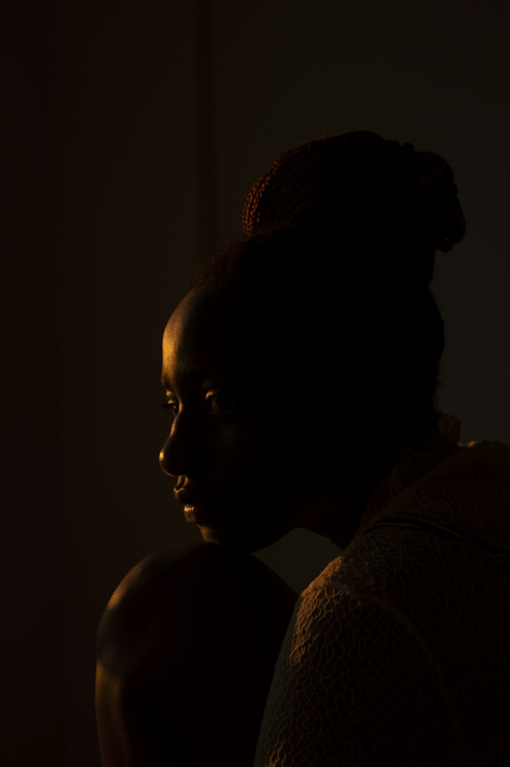 Une femme assise dans une pièce sombre, la tête tournée sur le côté