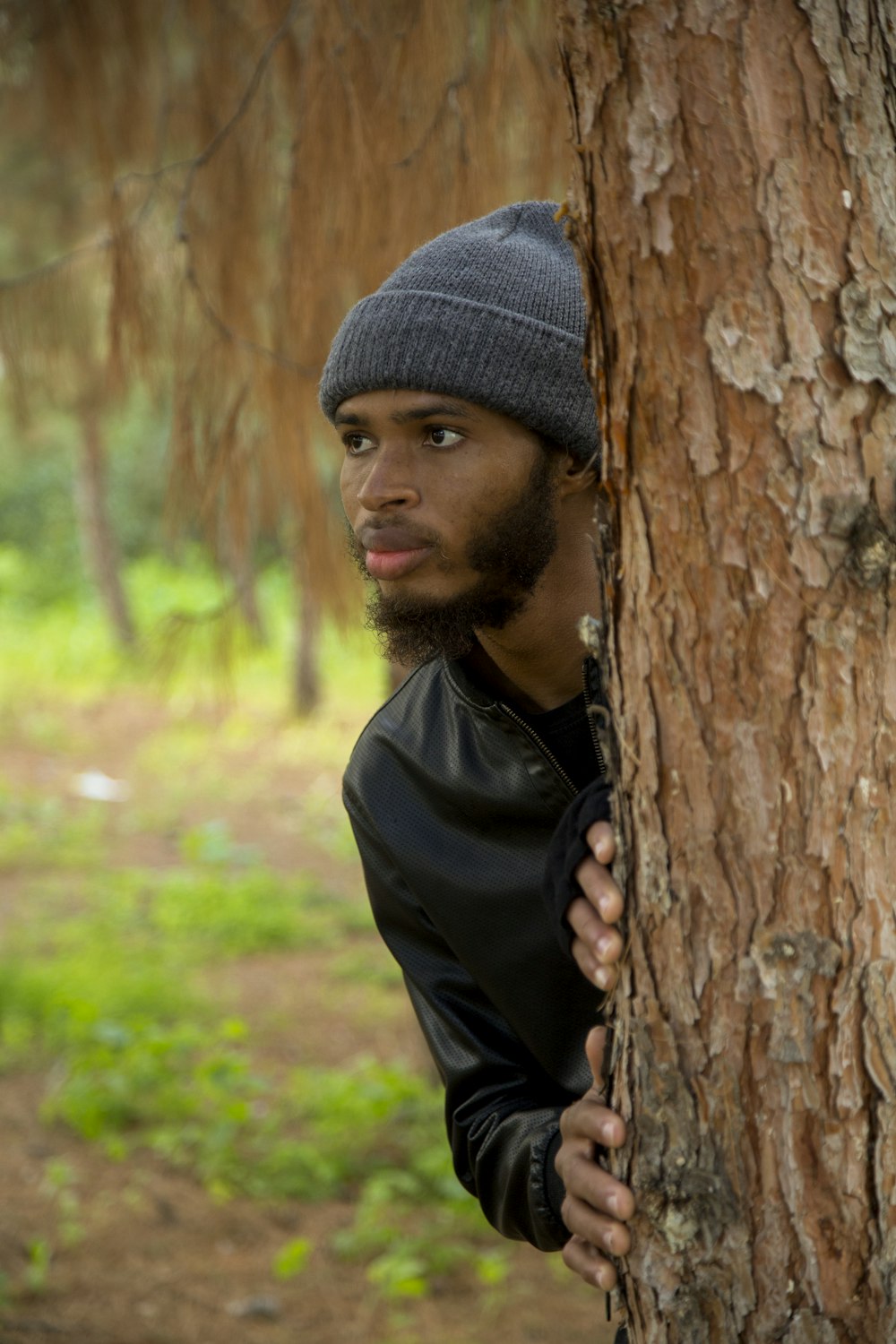 a man with a beard and a beanie leaning against a tree