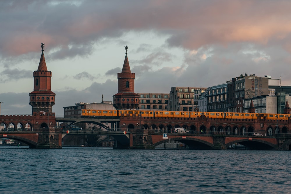 a yellow train traveling over a bridge next to tall buildings