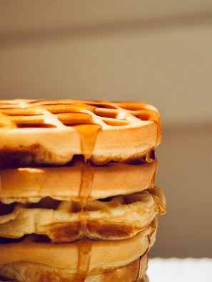 A stack of golden-brown waffles with syrup dripping down the sides, highlighting their crisp texture and inviting appearance.