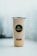 A clear cup filled with a light-colored beverage, featuring a black and gold logo with the word 'Majestea' on the front. The cup is sealed with a silver foil lid and has social media icons displayed below the logo. The background is softly blurred, creating a focus on the cup.