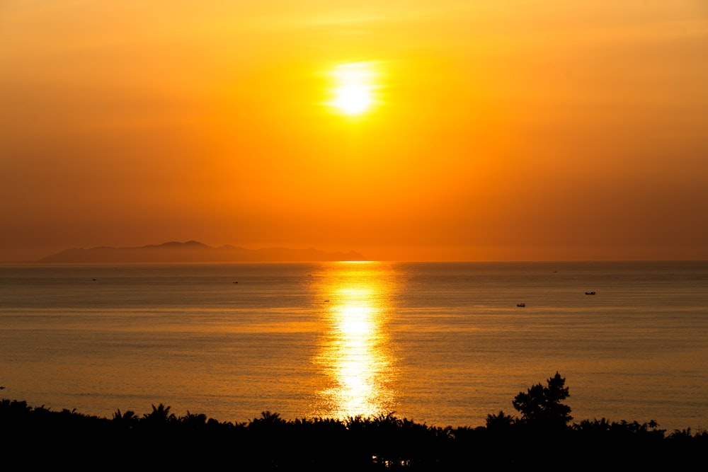 the sun is setting over the ocean with boats in the water