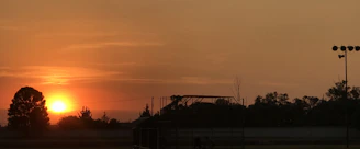 A warm, earthy-toned photograph of a vibrant Australian sunset over a rugged landscape with silhouetted trees.