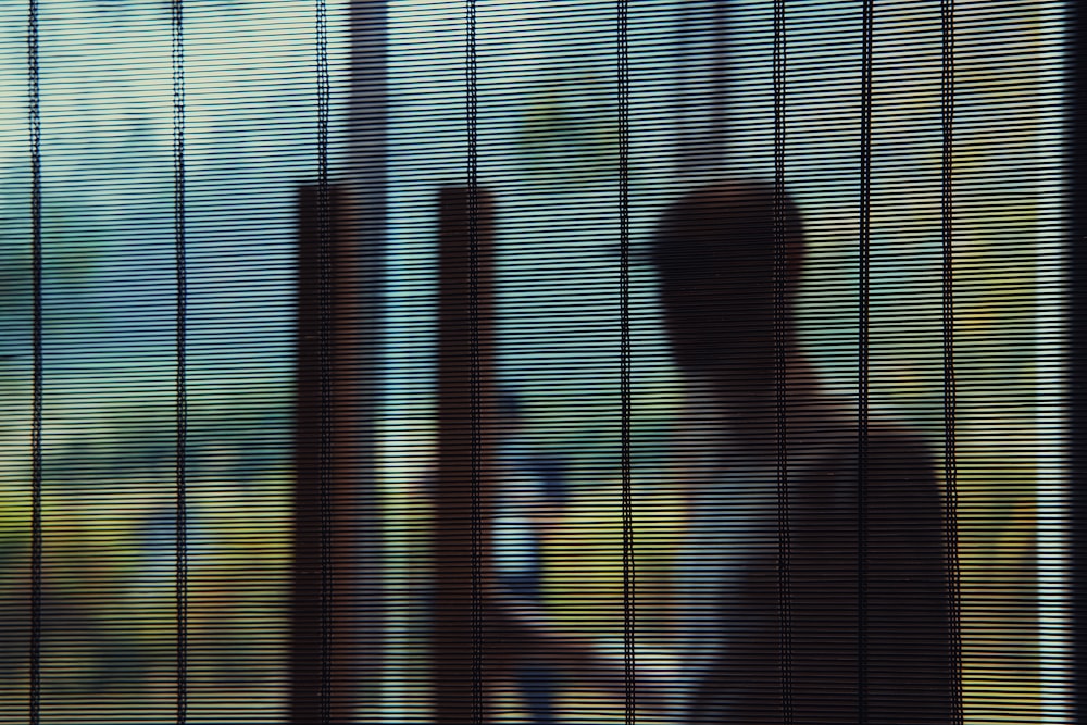 a person standing behind a window covered in blinds
