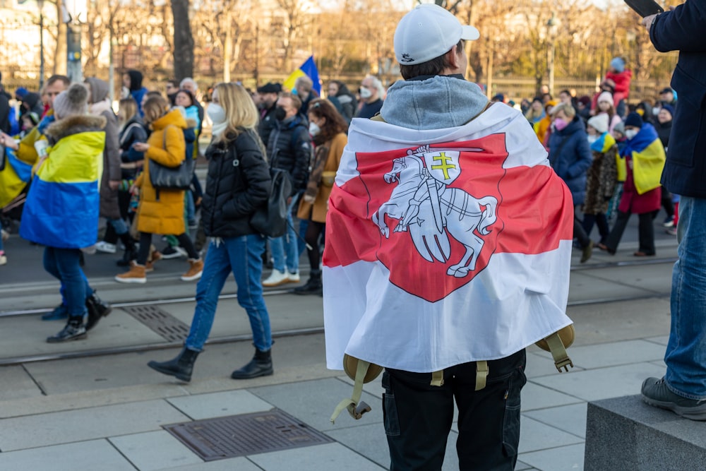 a man with a flag on his back standing in front of a crowd of people