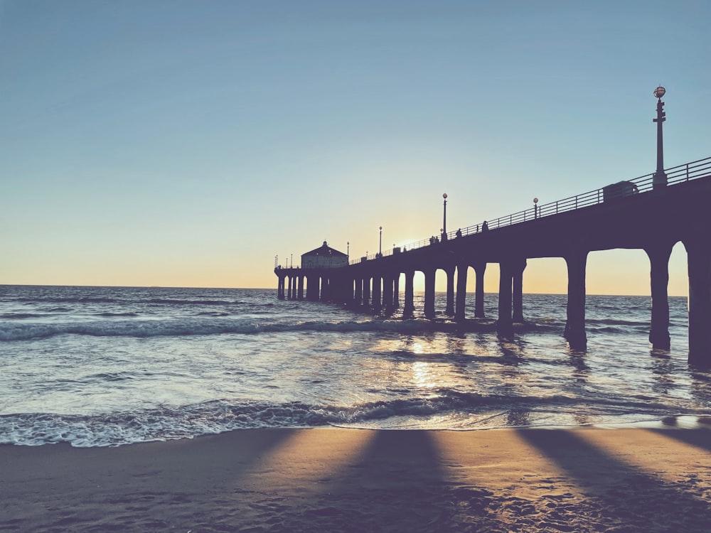 a pier on a beach with the sun setting