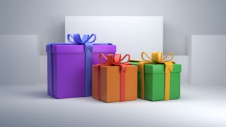 Three gift boxes of varying sizes are placed on a light surface, each adorned with a bow. The boxes are in purple, orange, and green, each wrapped with ribbons of contrasting colors: purple with blue, orange with red, and green with yellow. The background is minimalistic and grayish, adding a clean and elegant feel.