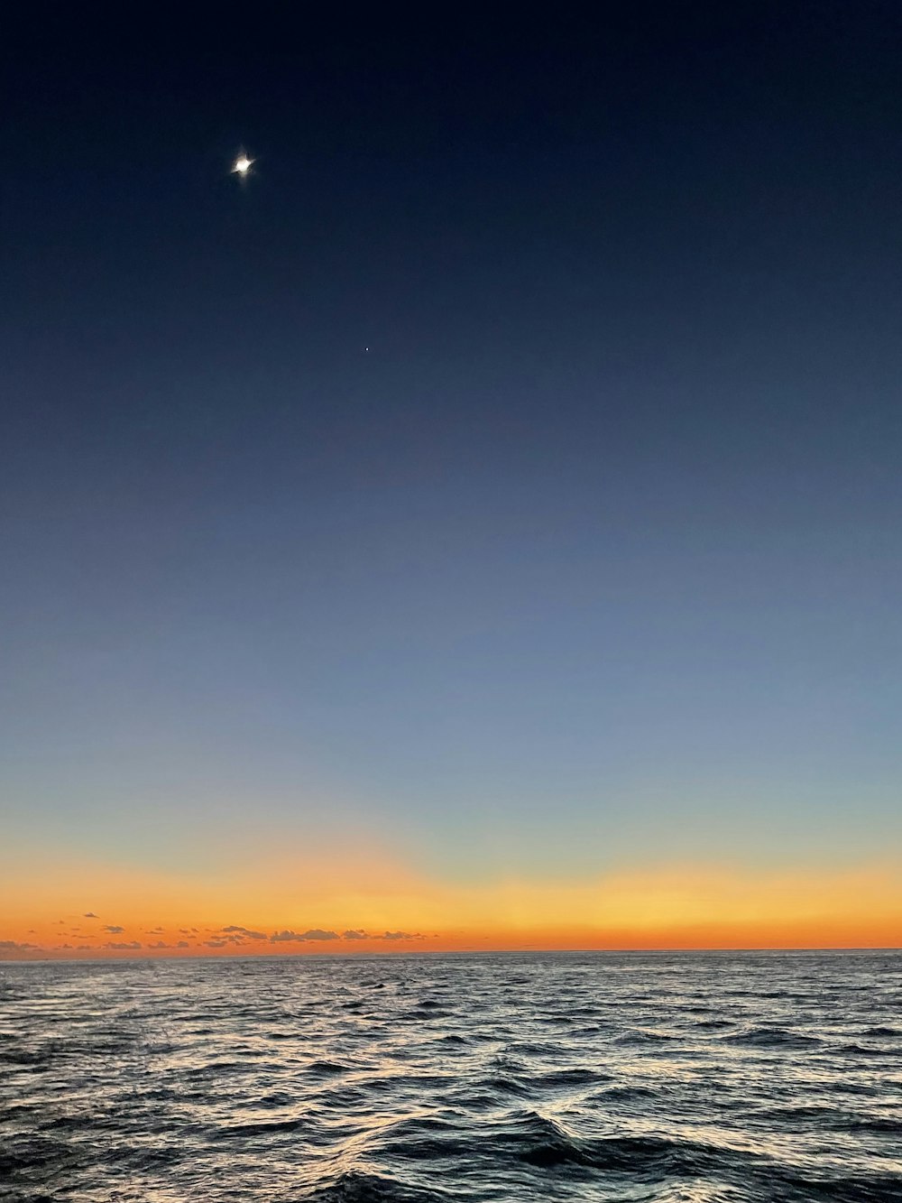 the sun is setting over the ocean with the moon in the sky