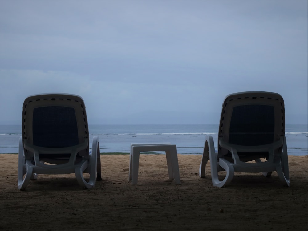 a couple of chairs sitting on top of a sandy beach