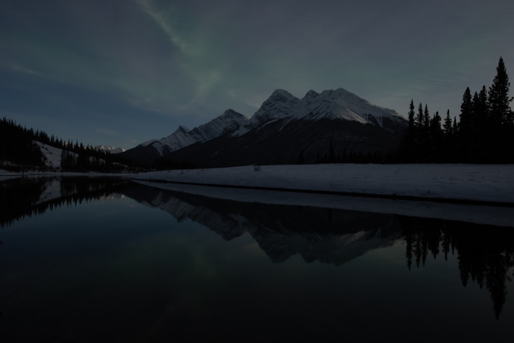 a lake surrounded by snow covered mountains under a cloudy sky