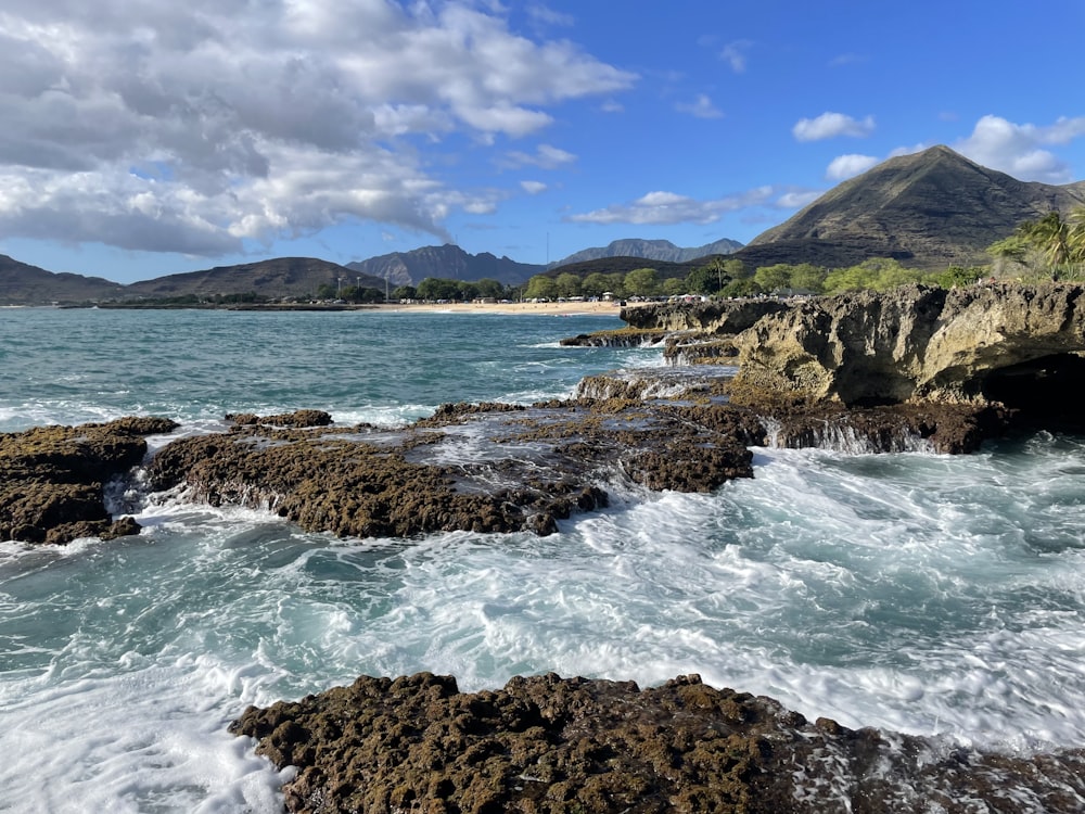 a rocky shore with a body of water and mountains in the background