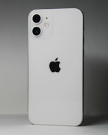 A white smartphone featuring a dual-camera setup in the upper left corner and a prominent black apple logo in the center. The device is positioned against a gradient gray background.