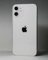 A white smartphone featuring a dual-camera setup in the upper left corner and a prominent black apple logo in the center. The device is positioned against a gradient gray background.