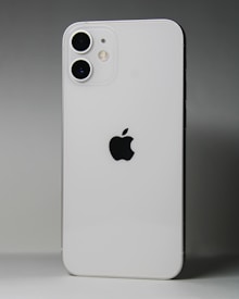 A white smartphone featuring a dual-camera setup in the upper left corner and a prominent black apple logo in the center. The device is positioned against a gradient gray background.