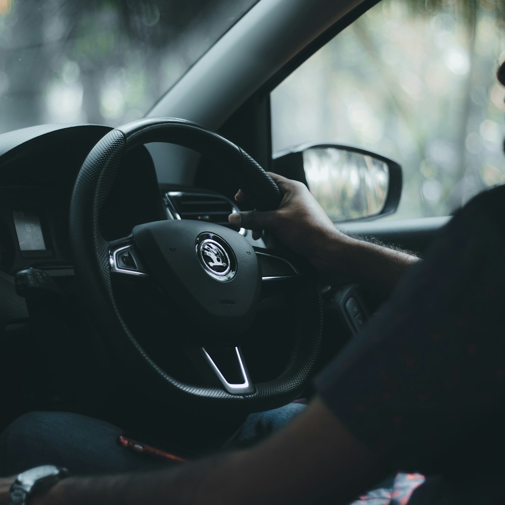 a man driving a car with his hand on the steering wheel