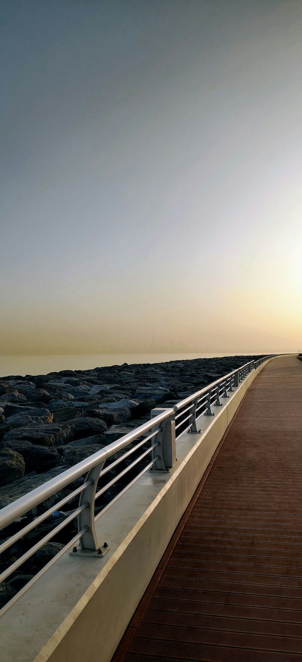 a wooden walkway next to the ocean at sunset
