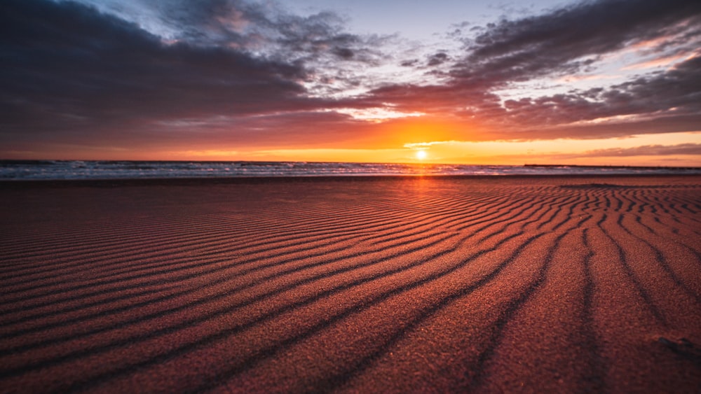 the sun is setting over the beach and the sand is wavy