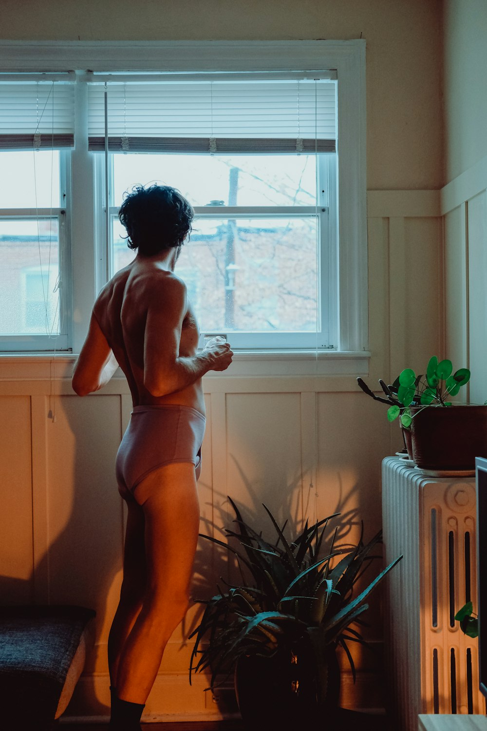 a woman standing in front of a window next to a plant