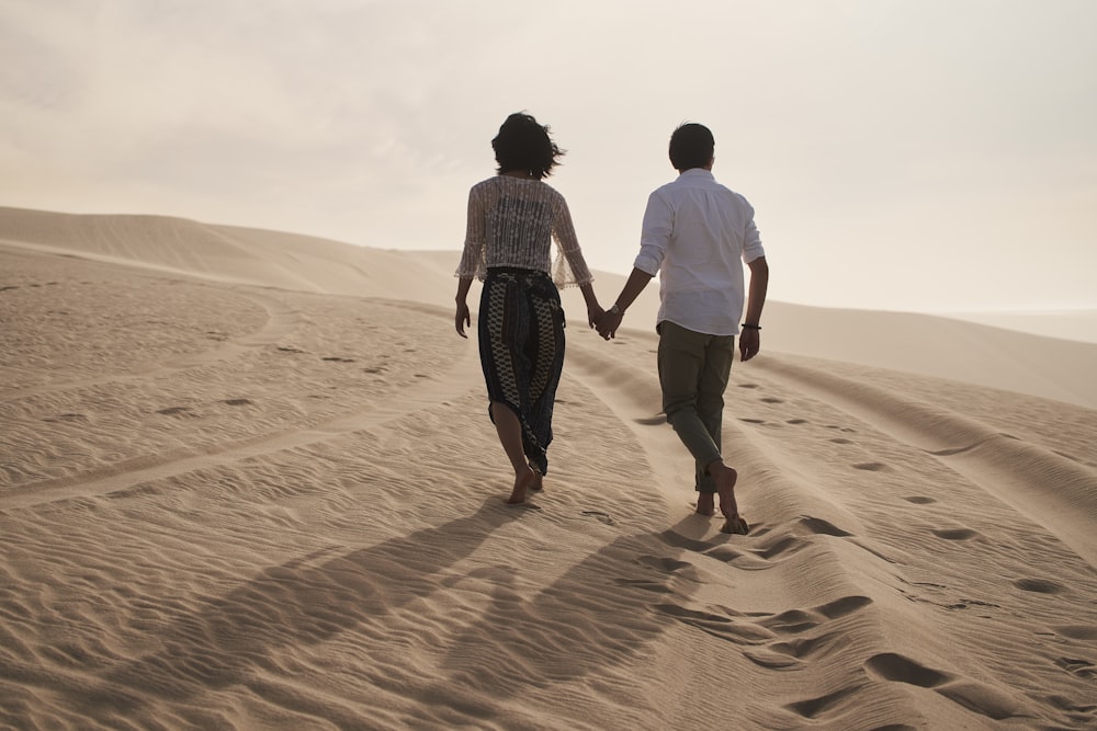 a man and a woman walking in the sand holding hands