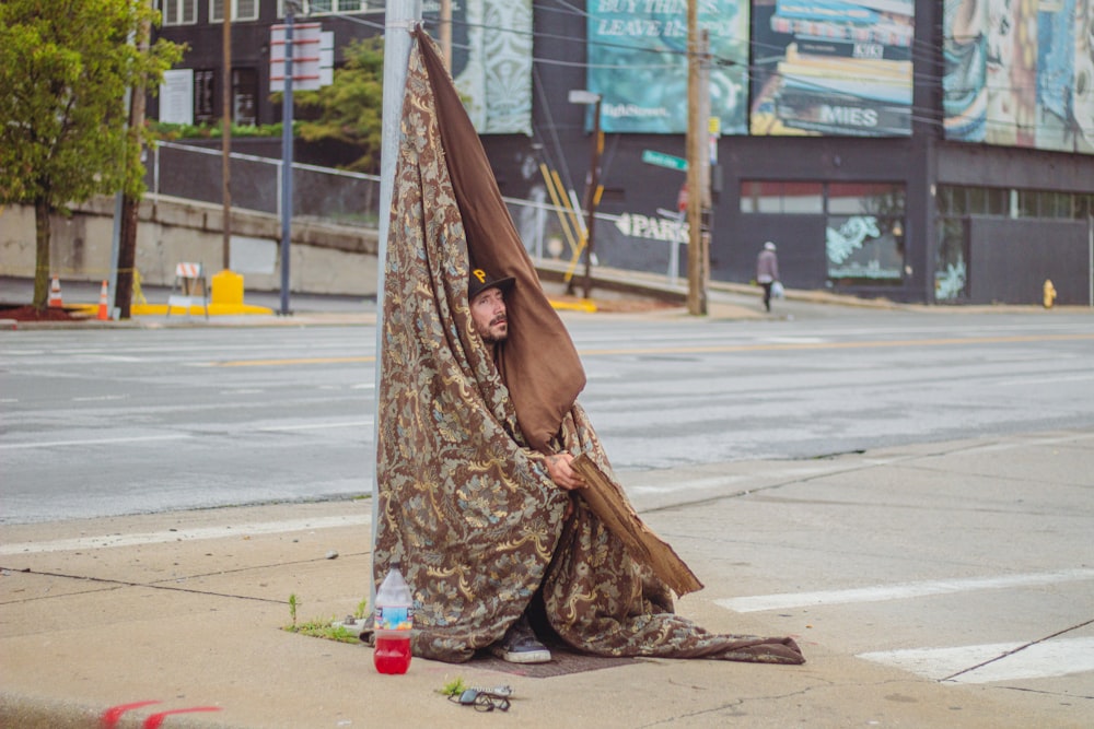 a man wrapped in a blanket sitting on the side of a road