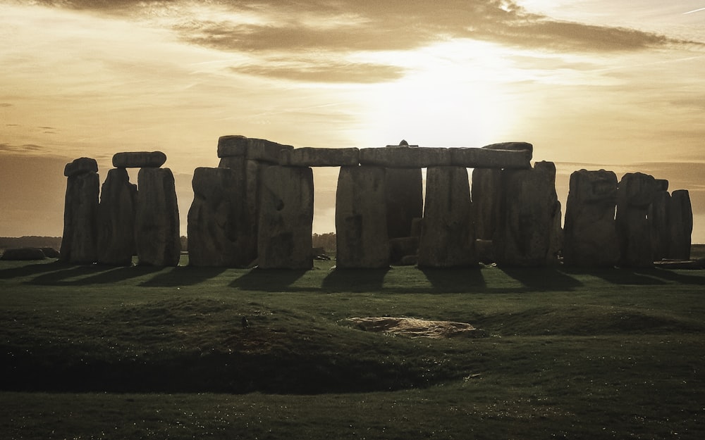 um stonehenge em um campo com o sol se pondo atrás dele