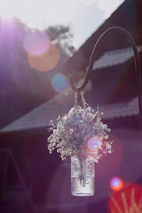A delicate hanging glass flower vase catching sunlight on a porch.