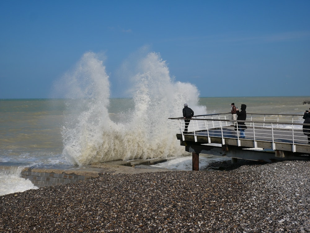 a group of people standing on a pier next to the ocean