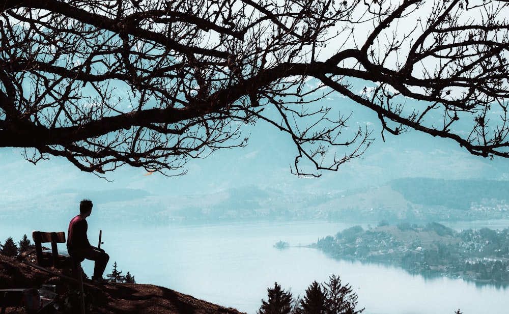 a man sitting on top of a hill next to a tree