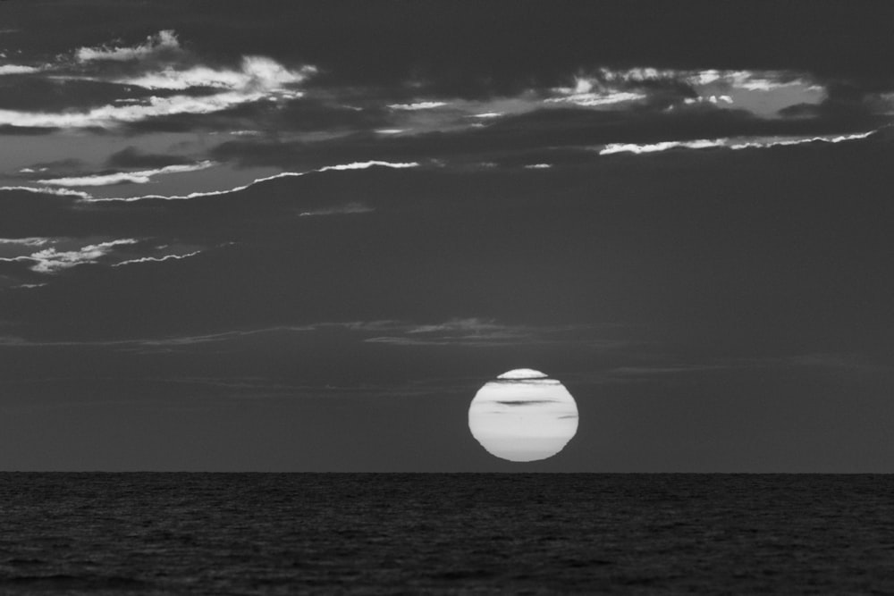 a black and white photo of the sun setting over the ocean