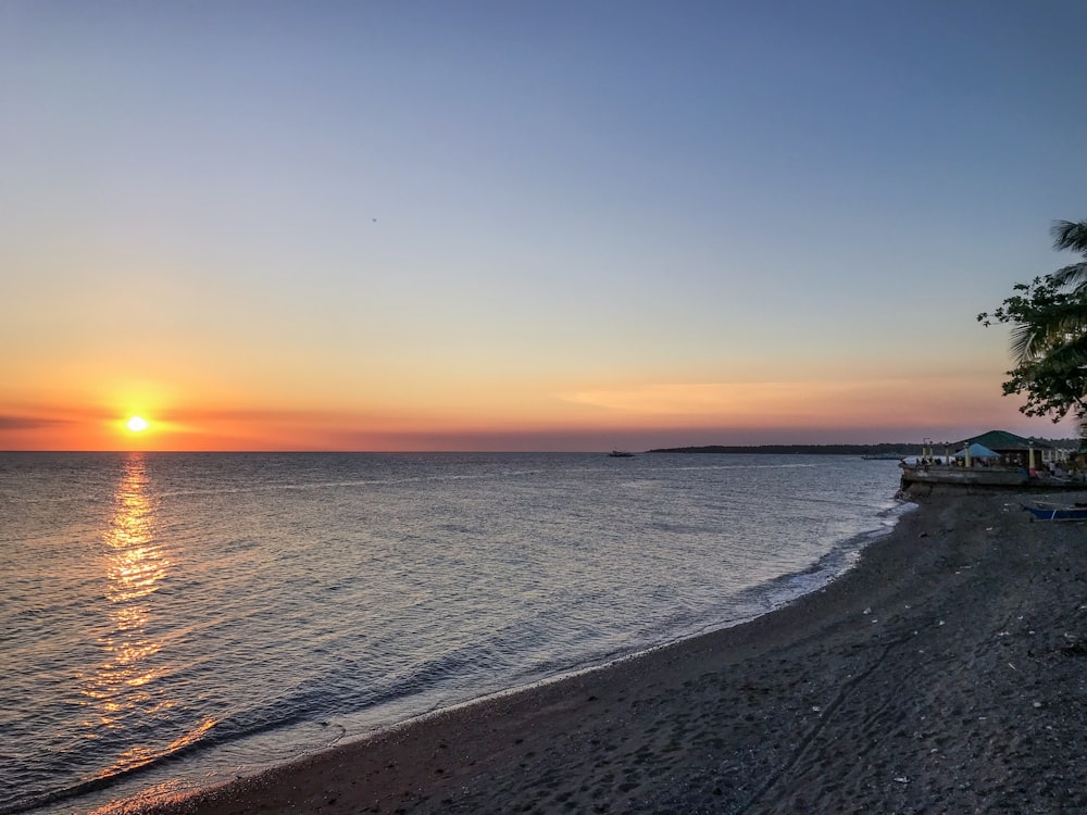 the sun is setting over the water at the beach