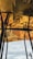 A reflective ceiling panel with a golden and bronze color palette creates an intricate pattern. Steel beams vertically intersect the reflection, and below, a cloudy sky is visible.