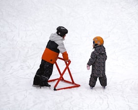 a couple of kids standing on top of a snow covered slope