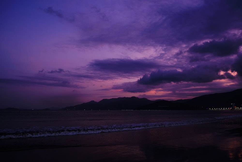 a purple sky over a beach with a mountain in the background