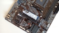 A close-up view of a computer motherboard featuring various components like a Kingston NVMe SSD, RAM slots, and a GIGABYTE logo. The board has intricate circuitry and connectors such as PCIe slots and capacitors.