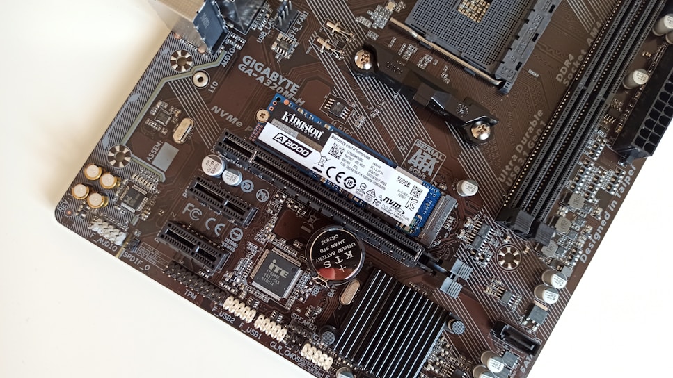 A close-up view of a computer motherboard featuring various components like a Kingston NVMe SSD, RAM slots, and a GIGABYTE logo. The board has intricate circuitry and connectors such as PCIe slots and capacitors.