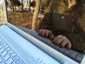 A close-up of a person typing on a laptop outdoors.