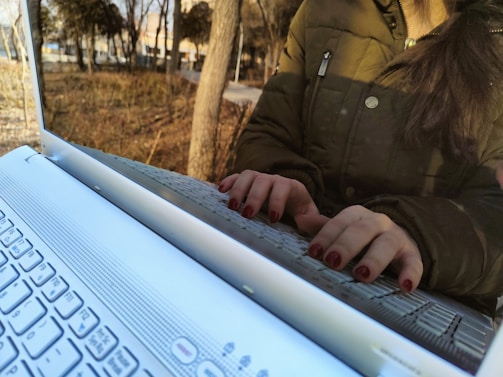 A close-up of a person typing on a laptop outdoors.