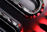Curved metallic and glossy elements intertwine with smooth, reflective surfaces, displaying a sleek, high-tech appearance. The image incorporates sharp contrasts between dark and light sections, with striking red accents providing a bold visual impact.