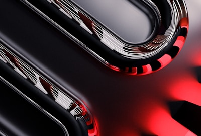 Curved metallic and glossy elements intertwine with smooth, reflective surfaces, displaying a sleek, high-tech appearance. The image incorporates sharp contrasts between dark and light sections, with striking red accents providing a bold visual impact.